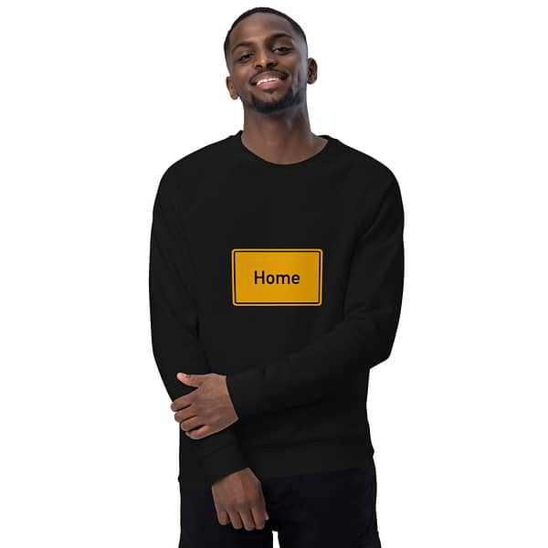 Ein Mann trägt ein schwarzes Unisex-Bio-Raglan-Pullover-Sweatshirt mit der Aufschrift „Home“ darauf.