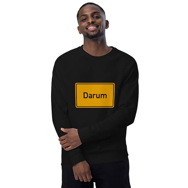 Ein Mann trägt ein schwarzes Unisex-Bio-Raglan-Pullover-Sweatshirt mit der Aufschrift „darum“.